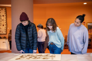 Three people looking down at a piece of artwork lying on a table.