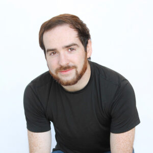 Headshot of Adam Ross leaning forward and smiling softly at the camera