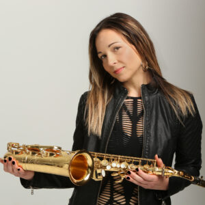 Woman posing in front of a white background, holding a saxophone in front of her