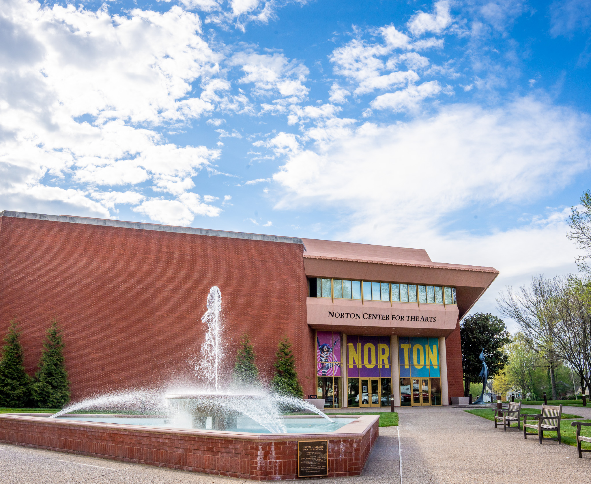 The front of the Norton Center, with the fountain in the foreground and the Noton Center entrance behind it. Blue sky with clouds behind the building.