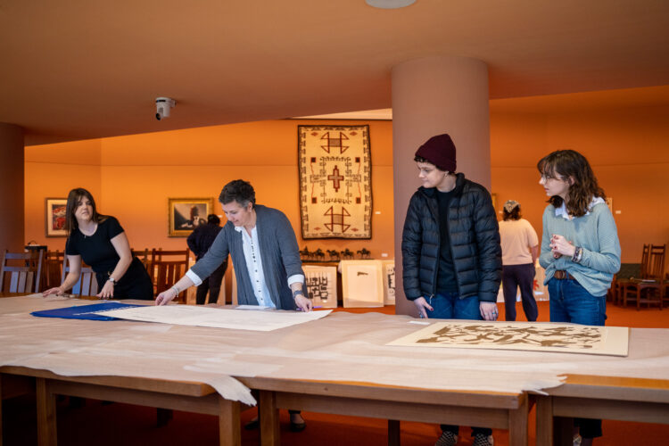 Professor Amy Frederick And Her Students Viewing The Peace Portfolio On A Table.