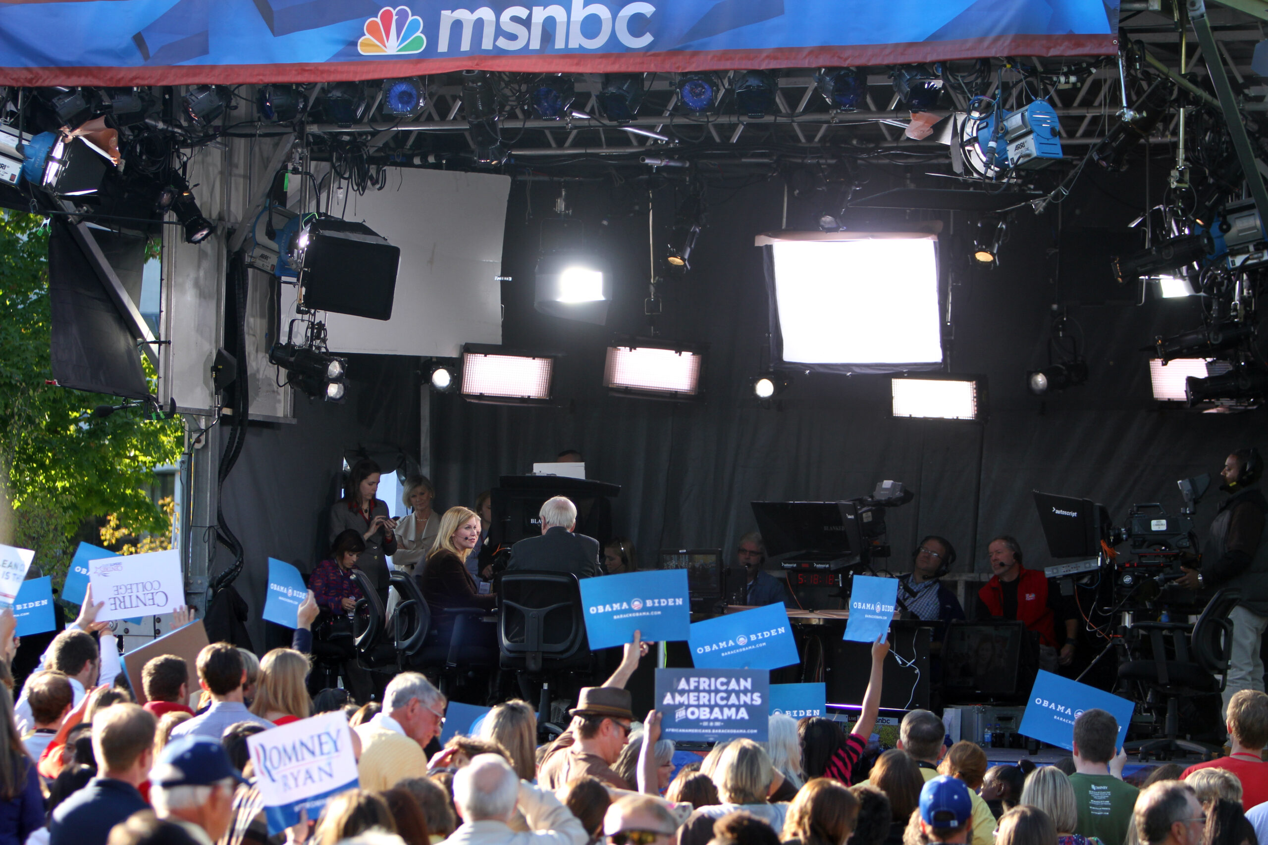 People holding political signs while MSNBC records in their booth behind them