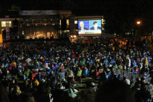 A crowd sits on the lawn of Centre College, watching the big screen