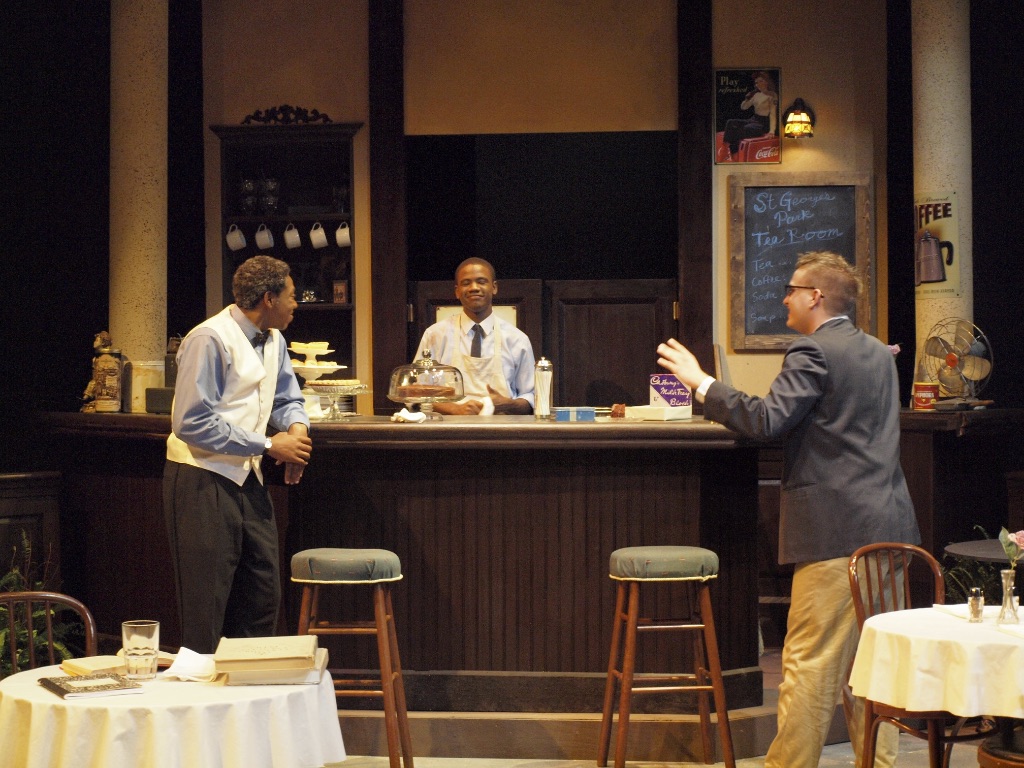 Three actors on stage of Master Harold. The scene is a cafe with one actor behind the counter and two in front, talking