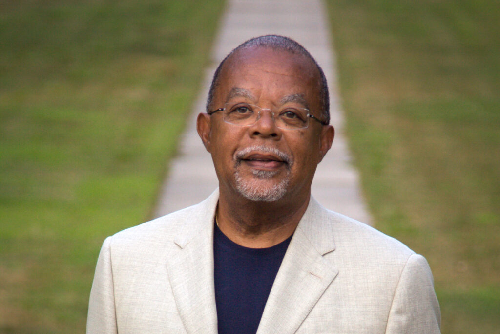 Henry Louis Gates, Jr. posing for a portrait in front of a concrete path and grassy lawn