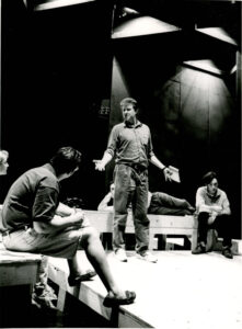Black and white photo of Patrick Kagan Moore standing on the weisiger stage, speaking with students who are sitting around him