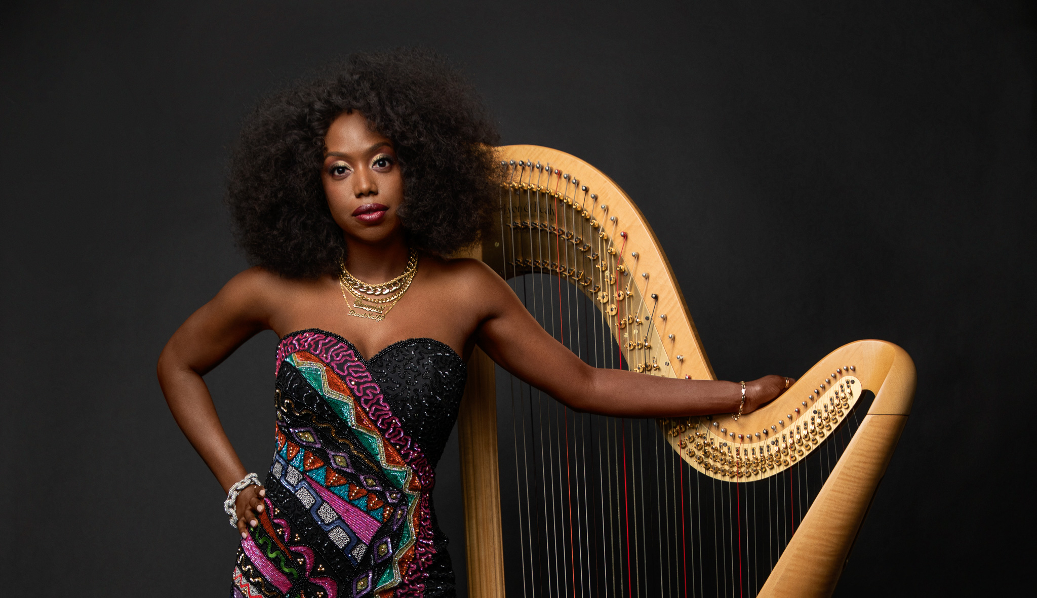 Brandee Younger stands in front of her harp with one arm draped over the instrument
