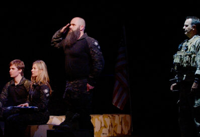 Four People Performing In Last Out. A Mom And Boy Sit To The Left Of The Frame, With A Soldier Saluting Behind Them And Another Soldier In Uniform Stands To The Right Of The Frame In Shadows.