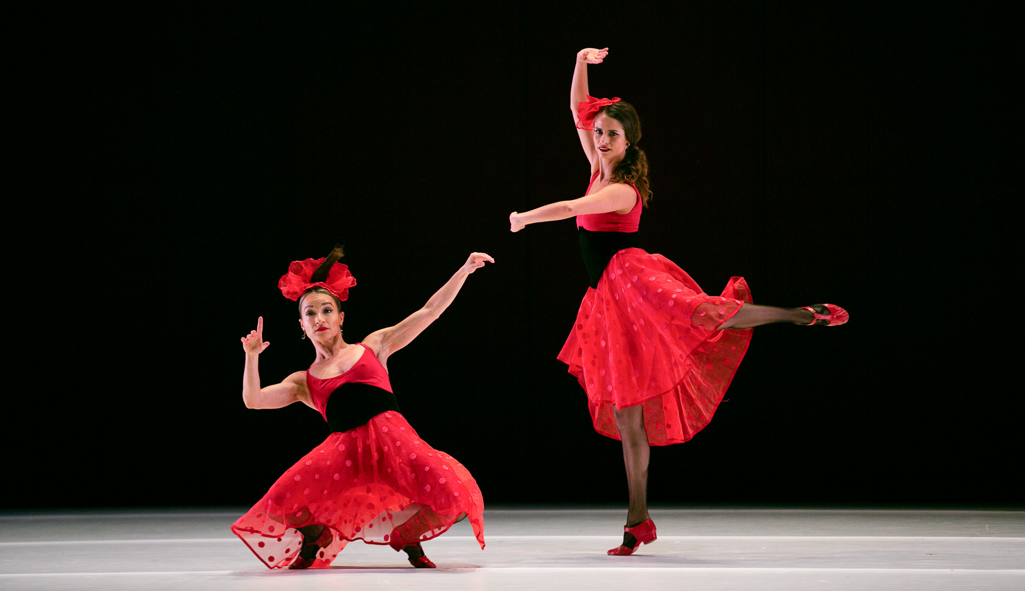 Dancers Lisa Borres and Maria Ambrose from the Paul Taylor Dance Company in red dress costumes dancing on stage.