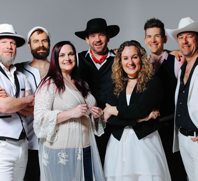 The Seven Wonders band members pose and smile against a gray background
