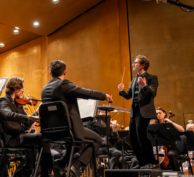 Teddy Abrams standing on a podium while conducting the Louisville Orchestra