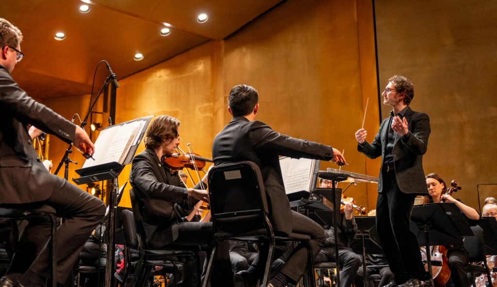 Teddy Abrams standing on a podium while conducting the Louisville Orchestra