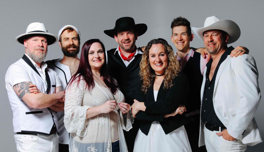 The Seven Wonders band members pose and smile against a gray background