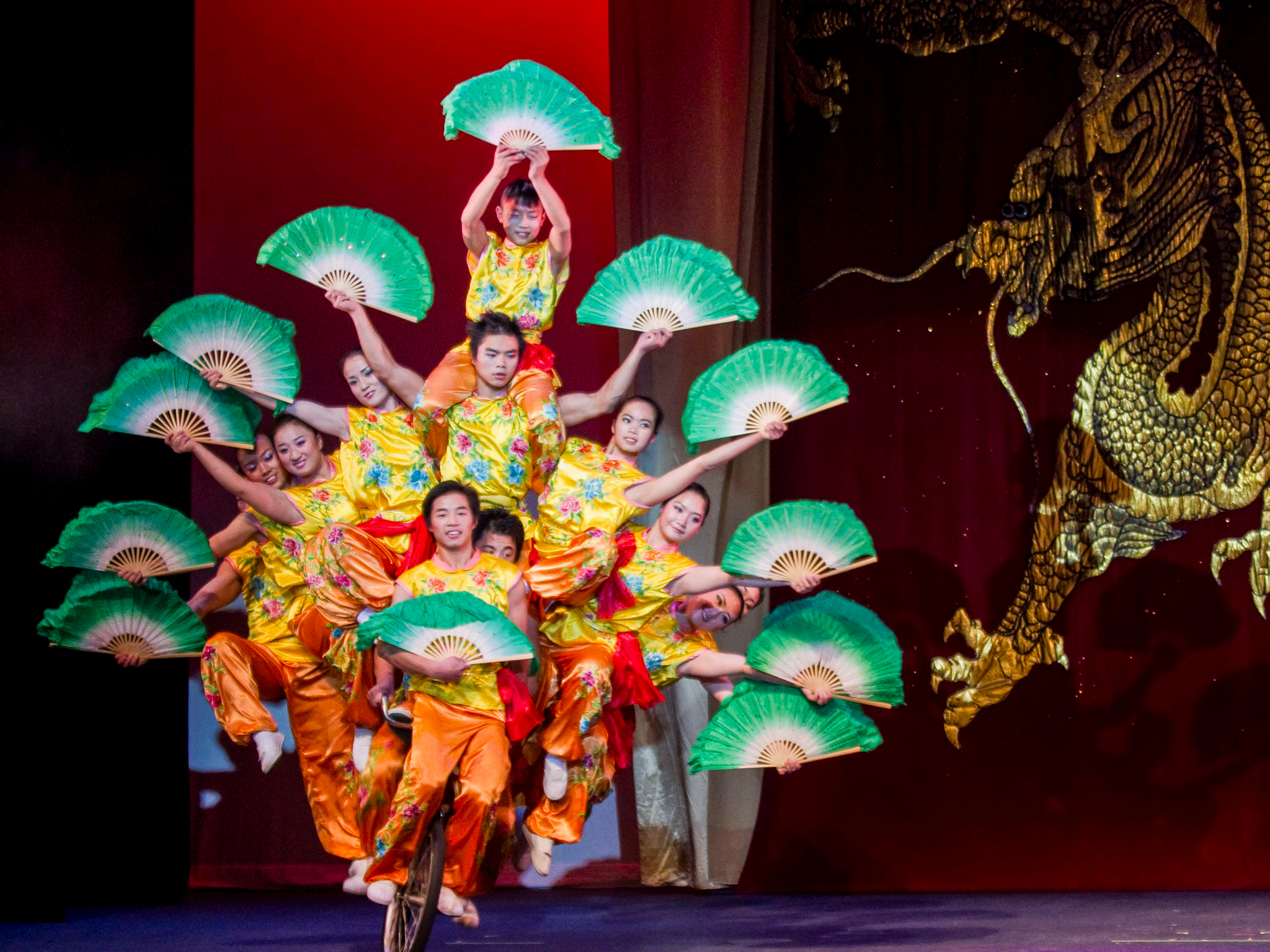 The Peking Acrobats stacked on one another's shoulders, holding colorful and fans