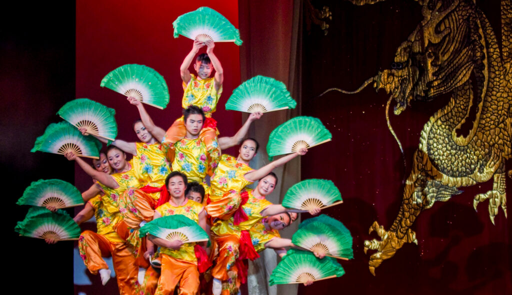 The Peking Acrobats stacked on one another's shoulders, holding colorful and fans