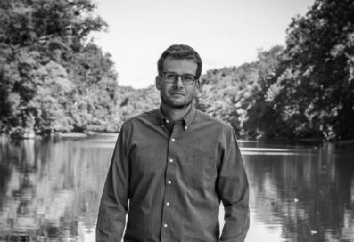 Black And White Portrait Of John Green Standing In Front Of A Lake