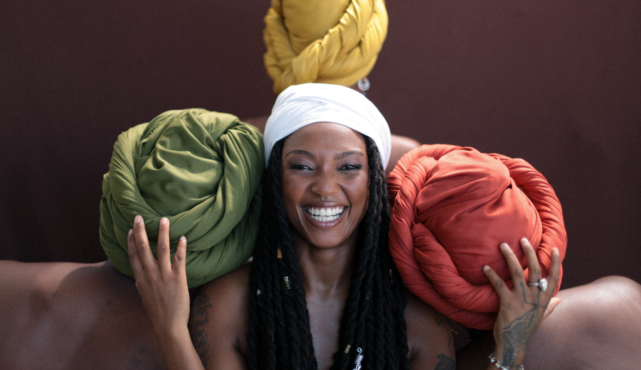Bia Ferreira smiling, holding her hands up. Side by side and behind her are 3 women facing away from the camera. The women are wearing head scarves in different colors