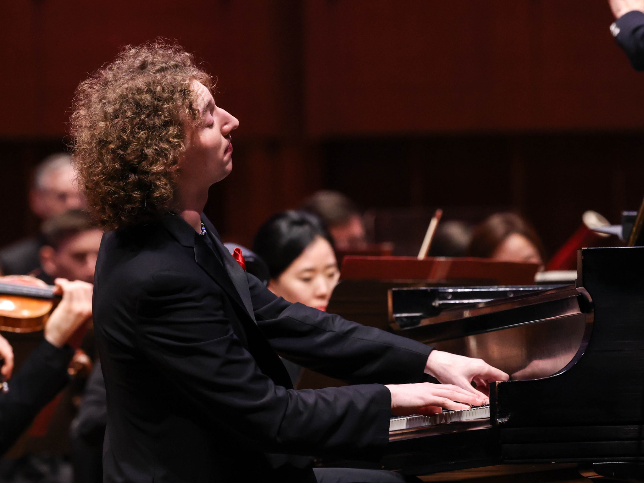 A side view of Michael Davidman playing piano in front of an orchestra.