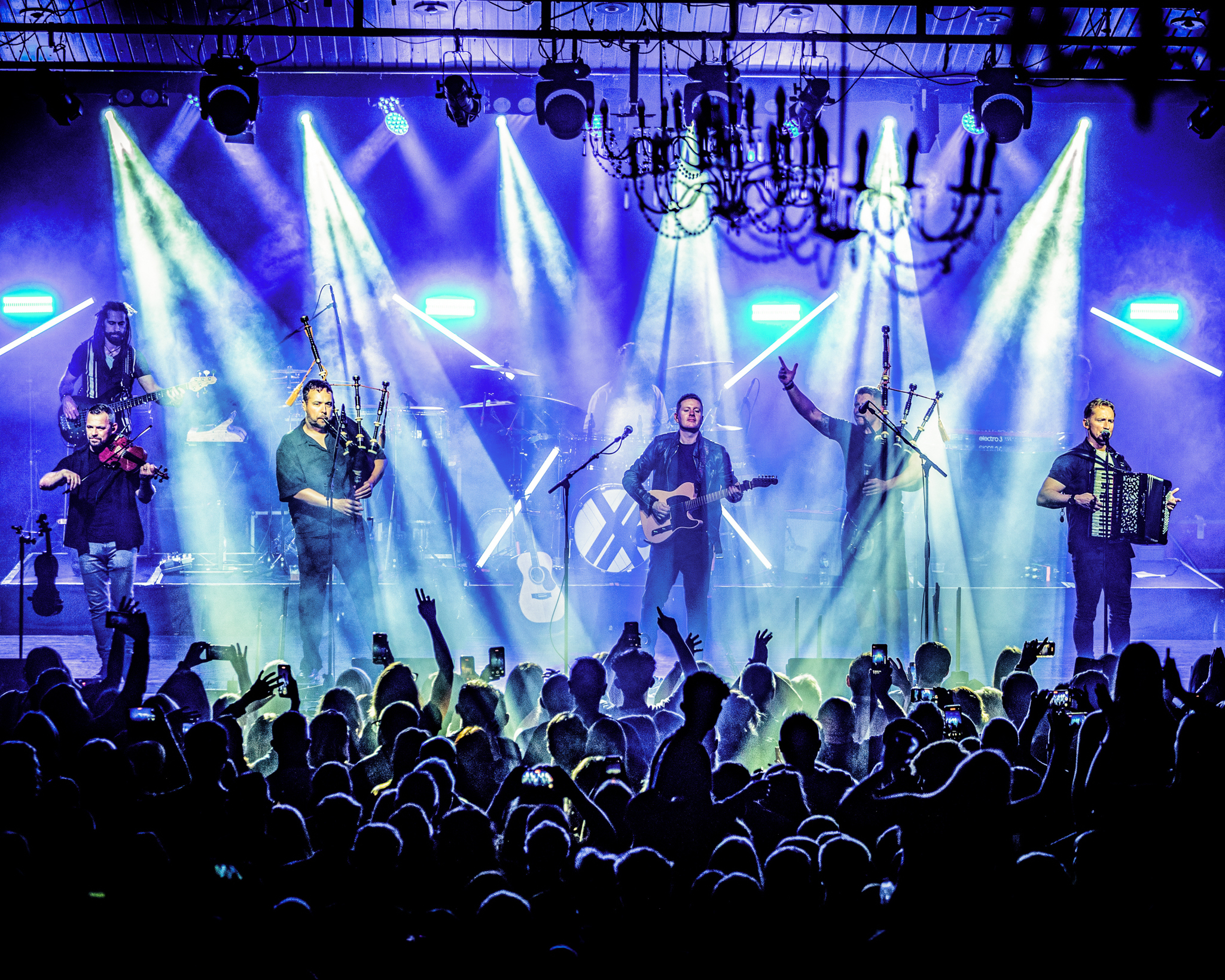 Members of the band Skerryvore performing on stage in front of a packed audience. Stage lights shine down on the performers.