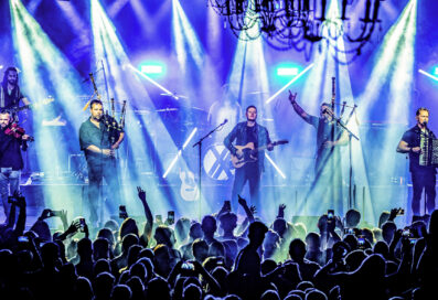 Members Of The Band Skerryvore Performing On Stage In Front Of A Packed Audience. Stage Lights Shine Down On The Performers.