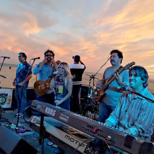 The Mystic band, performing music on a stage in front of a body of water and sunset